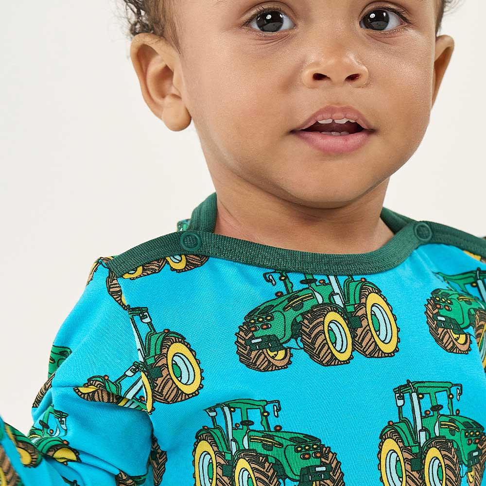 A young boy stood wearing a blue and green top with tractor print