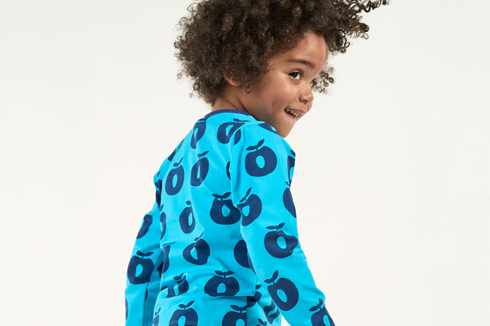 A young boy stood wearing a blue top with apple pattern