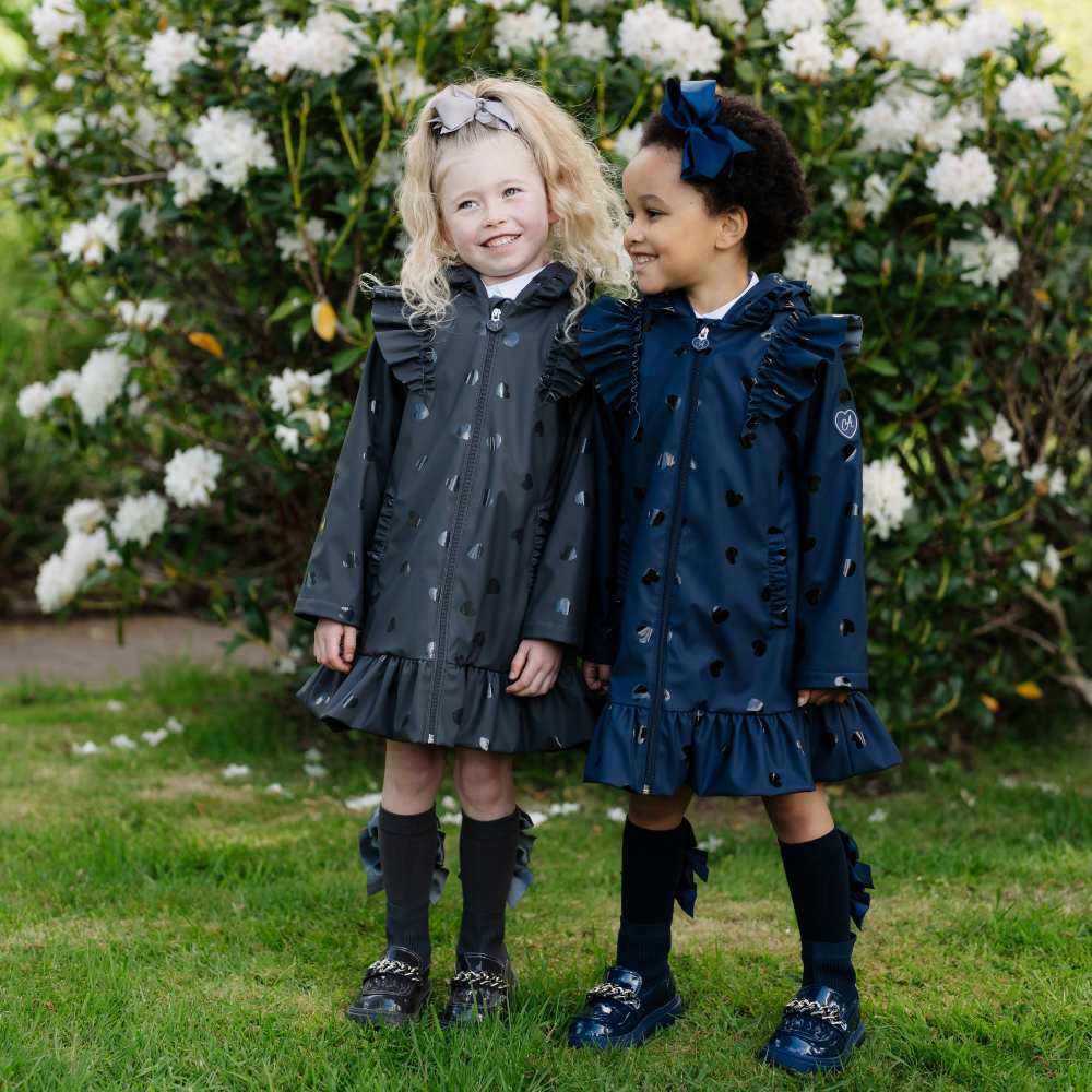 Twp girls stood outside in front of a bush covered in white flowers wearing Back to School outfits by A Dee 