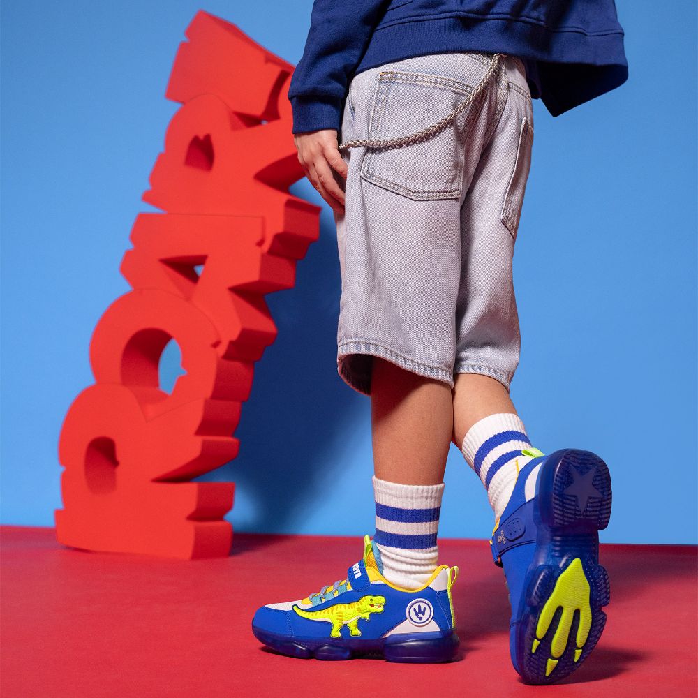 A boy wearing shorts and Istamax trainers stood beside a red ROAR! sign 