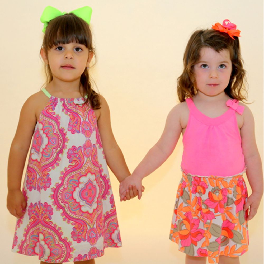 Two girls holding hands wearing brightly coloured summer outfits and hair bows 