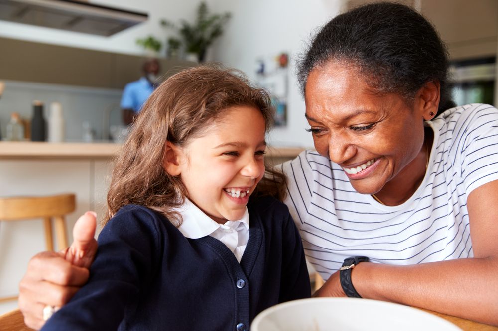 A woman smiling sat with a young smiling child in school uniform at a kitchen table