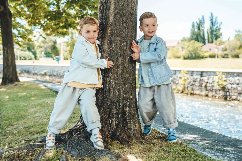 Two boys outside stood next to a large tree