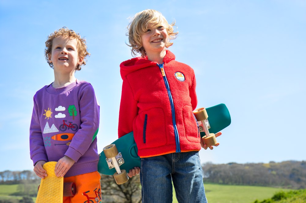 Two boys stood outside with skateboards wearing colourful outfits by Frugi