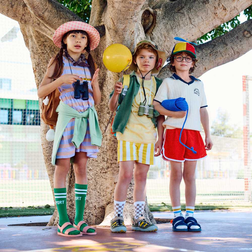 Three children stood outside under a tree wearing brightly coloured summer outfits and sandals by Gioseppo Kids 