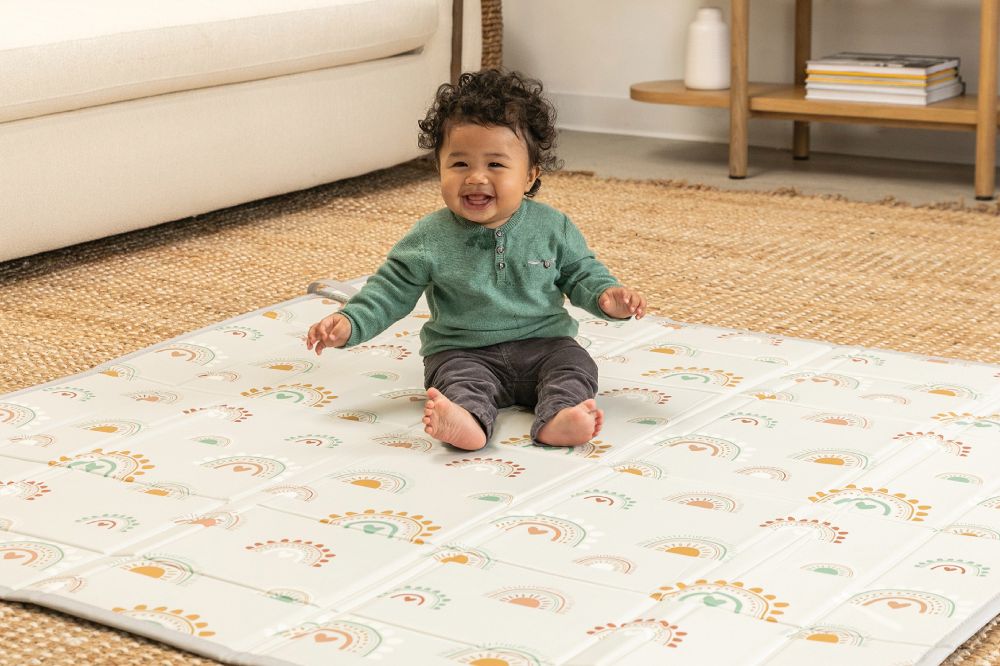 A baby sat on the floor on a rainbow print playmat by Infantino