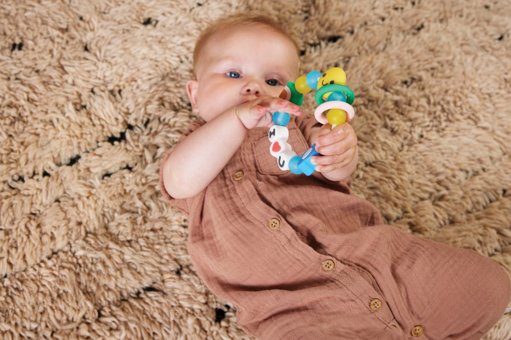 A baby lying on a rug on the floor playing with a teether by Infantino