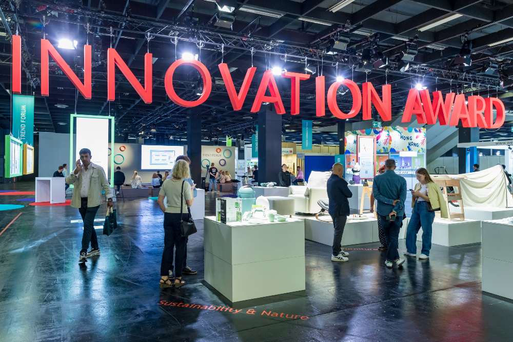 Inside an exhibition hall at Kind + Jugend with a red Innovation Award sign hanging from the ceiling