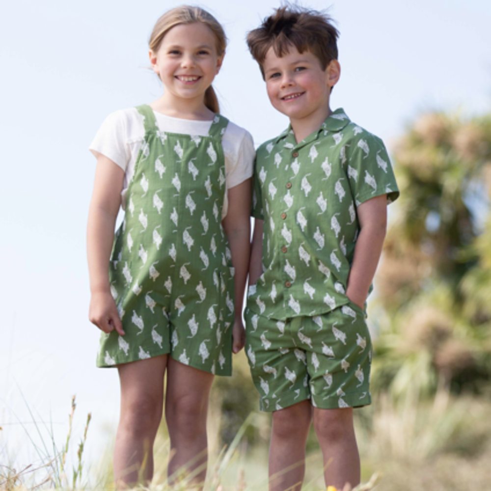 A young boy and girl stood outside wearing matching green summer outfits 
