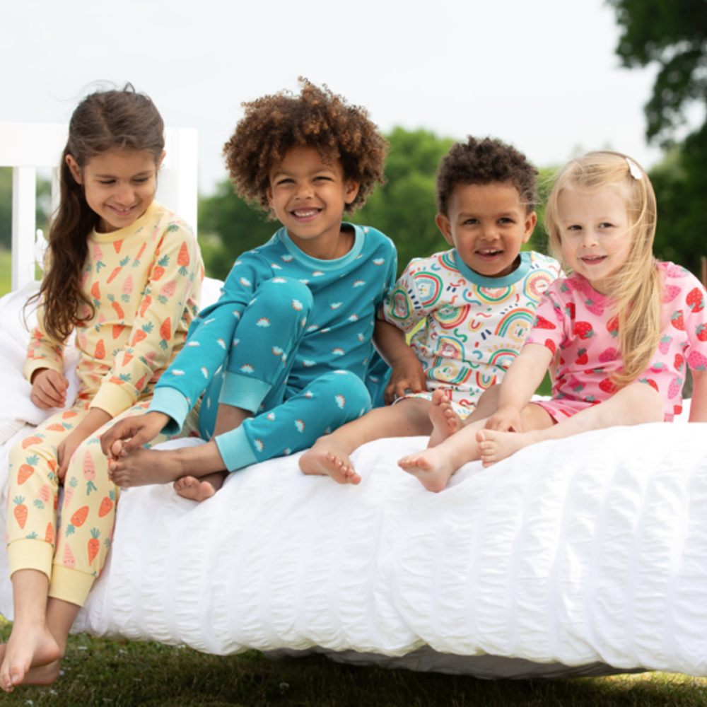 A group of children in pyjamas sat on a bed outside 