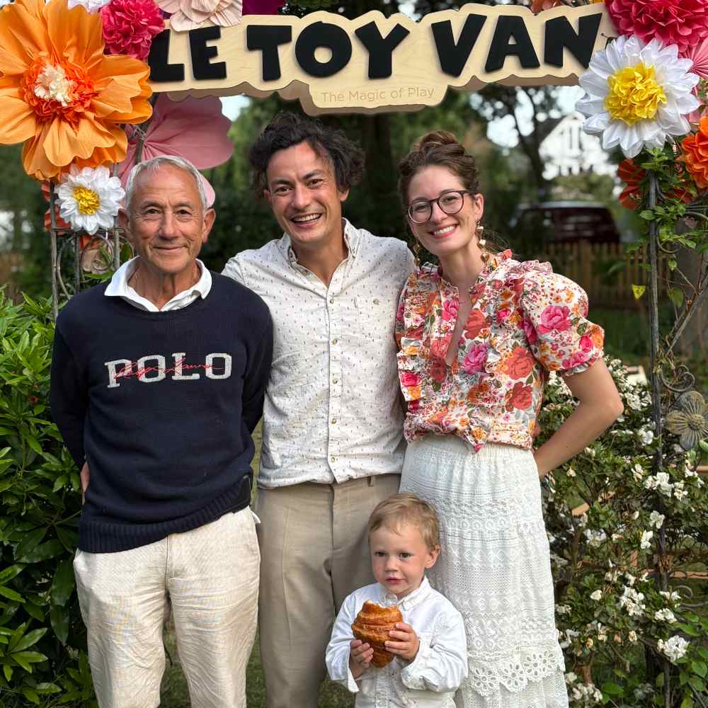 A group of people stood in front of a wall of flowers with a Le Toy Van sign 