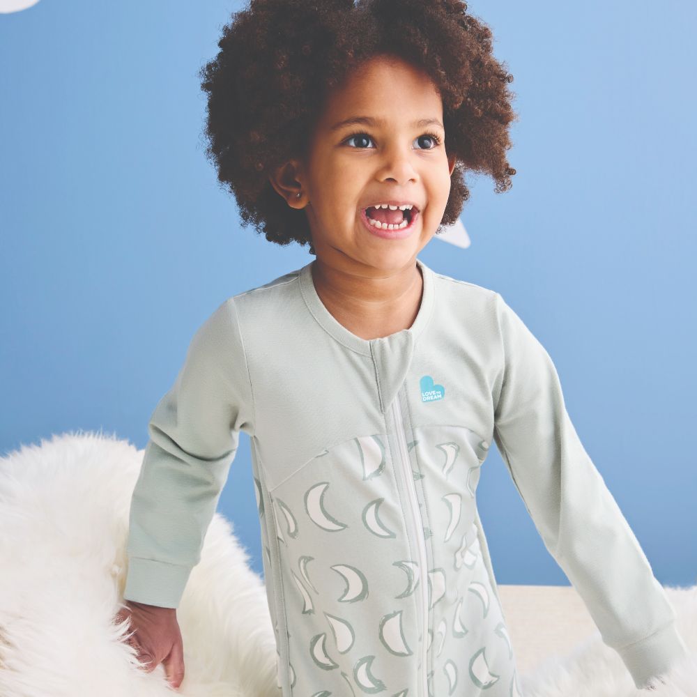 A young child against a blue background wearing a sleepsuit by Love to Dream