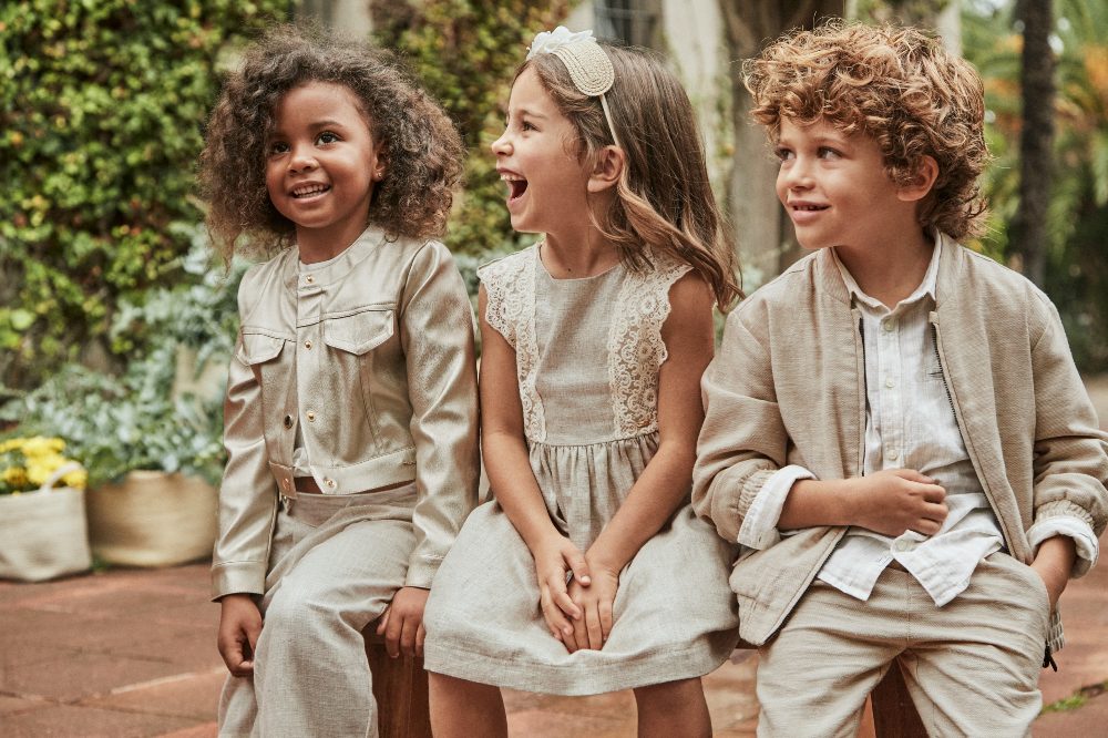 Three children sat outside on a wall in coordinating summer outfits