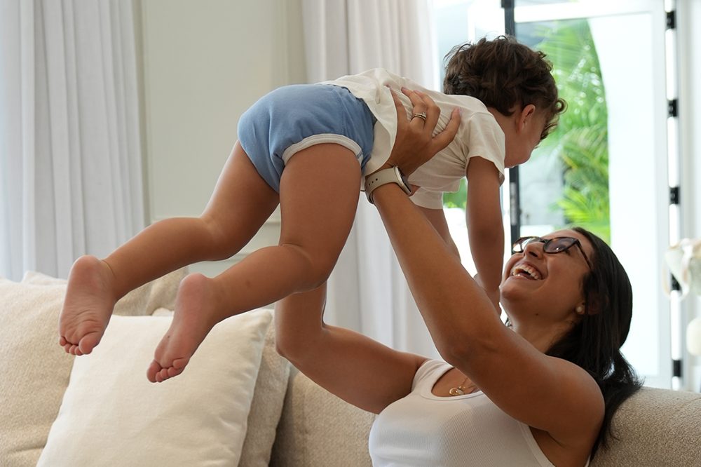 A woman lifting a toddler in the air wearing blue organic training pants by My Carry Potty