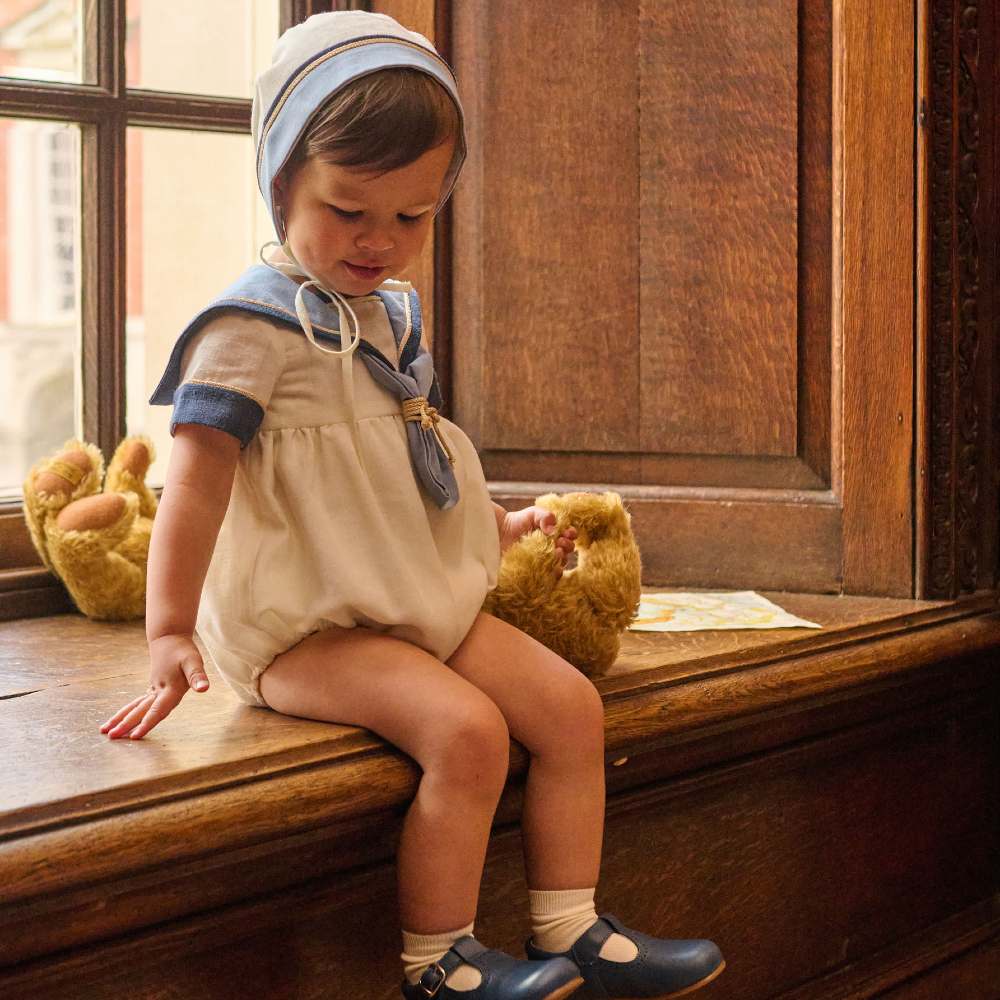 A child sat on a window ledge wearing a nautical inspired outfit and bonnet from the Pepa London x Historic Royal Palaces collection 