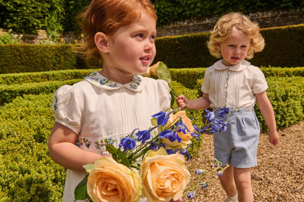 Two children in a garden wearing outfits from the Pepa London x Historic Royal Palaces