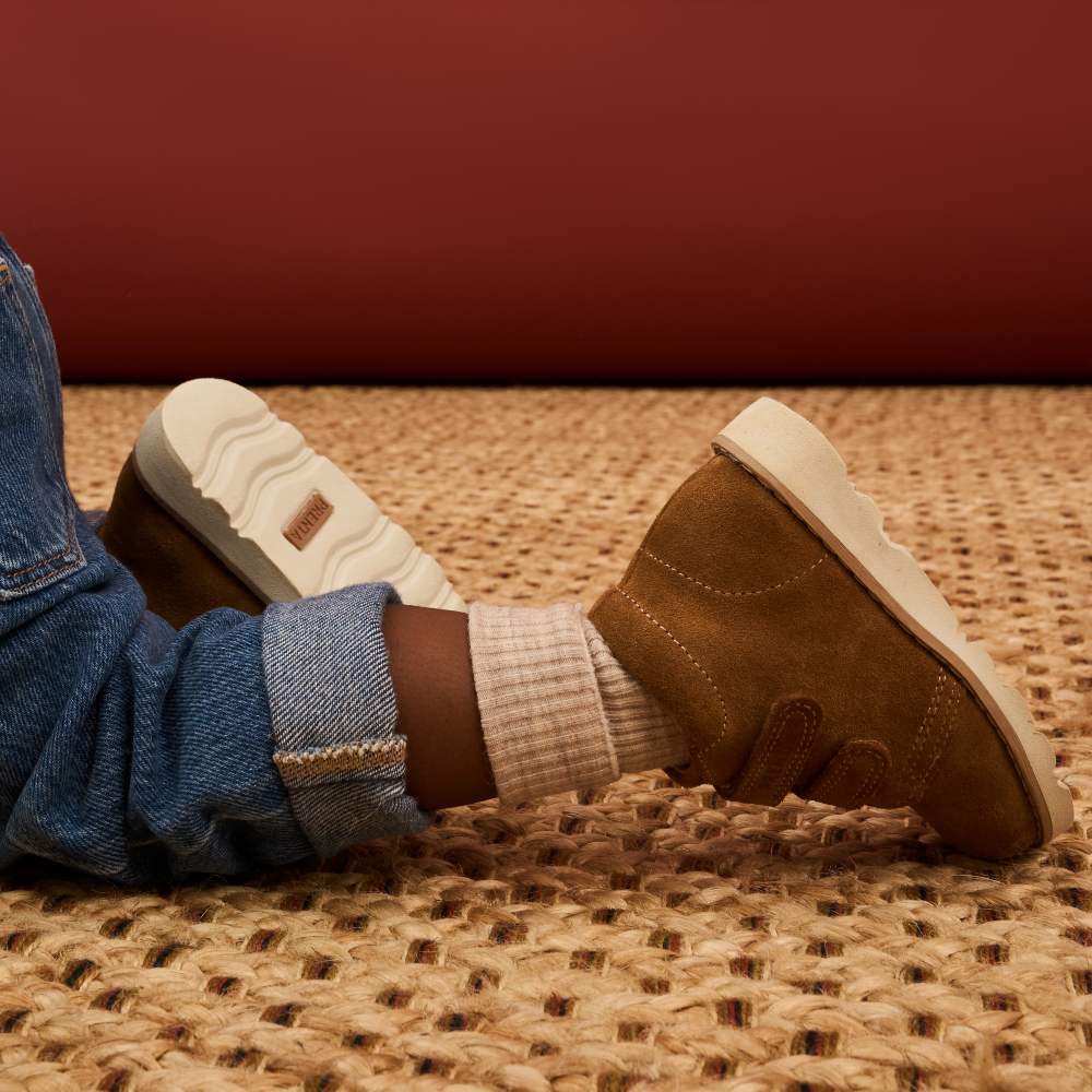 A child's legs shown crawling wearing brown suede boots on their feet