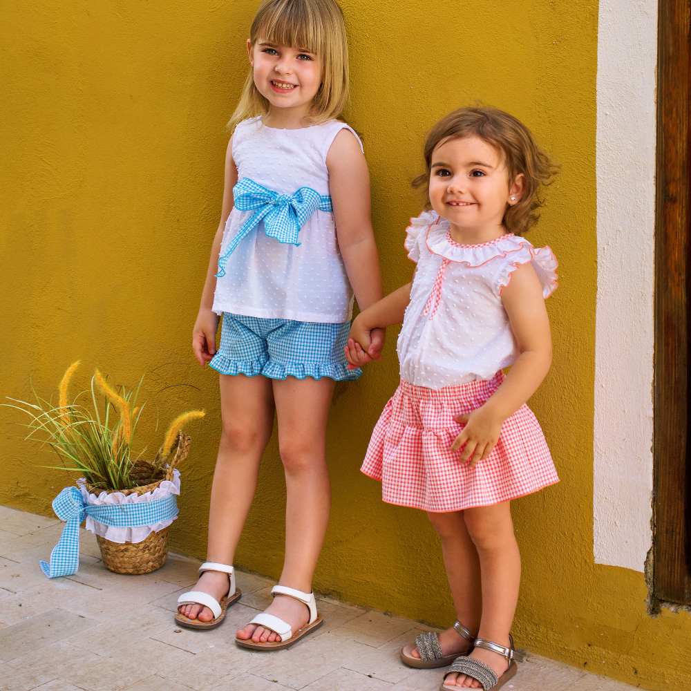 Two girls in summer outfits stood outside a mustard coloured building 