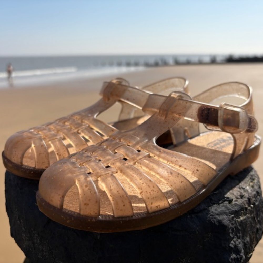 A pair of children's jelly shoes displayed on a post on a beach 
