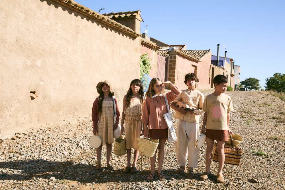 A group of children in summer outfits stood together outside an old building