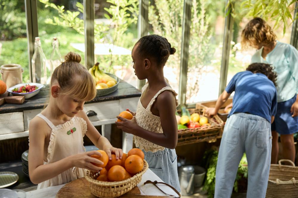Four children in a kitchen wearing summer outfits and sorting fruit and vegetables into baskets 