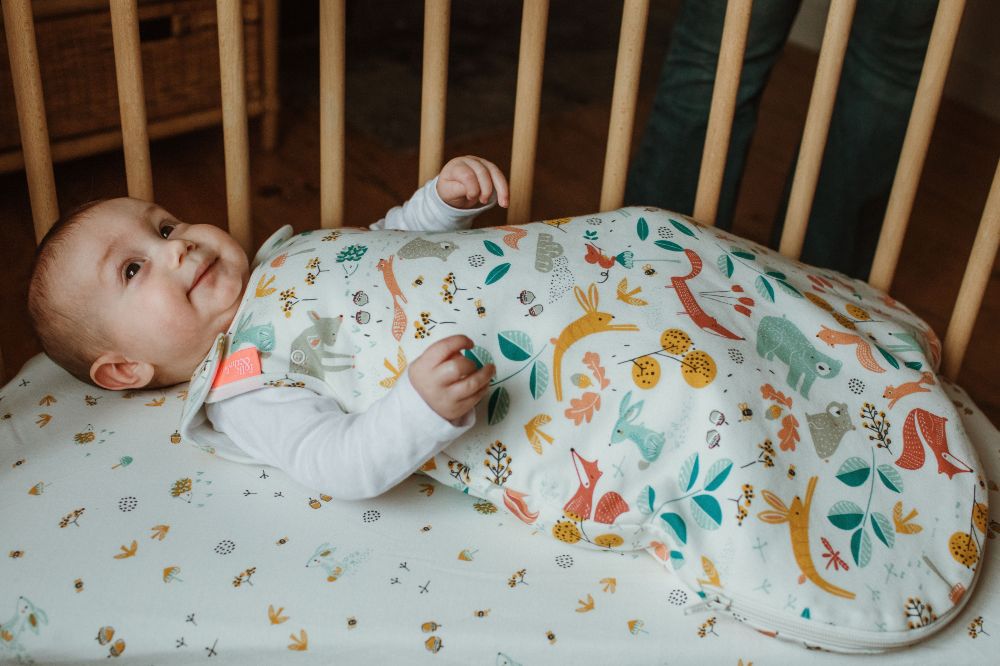 A baby lying in a crib wearing a sleeping bag by Folk & Thread