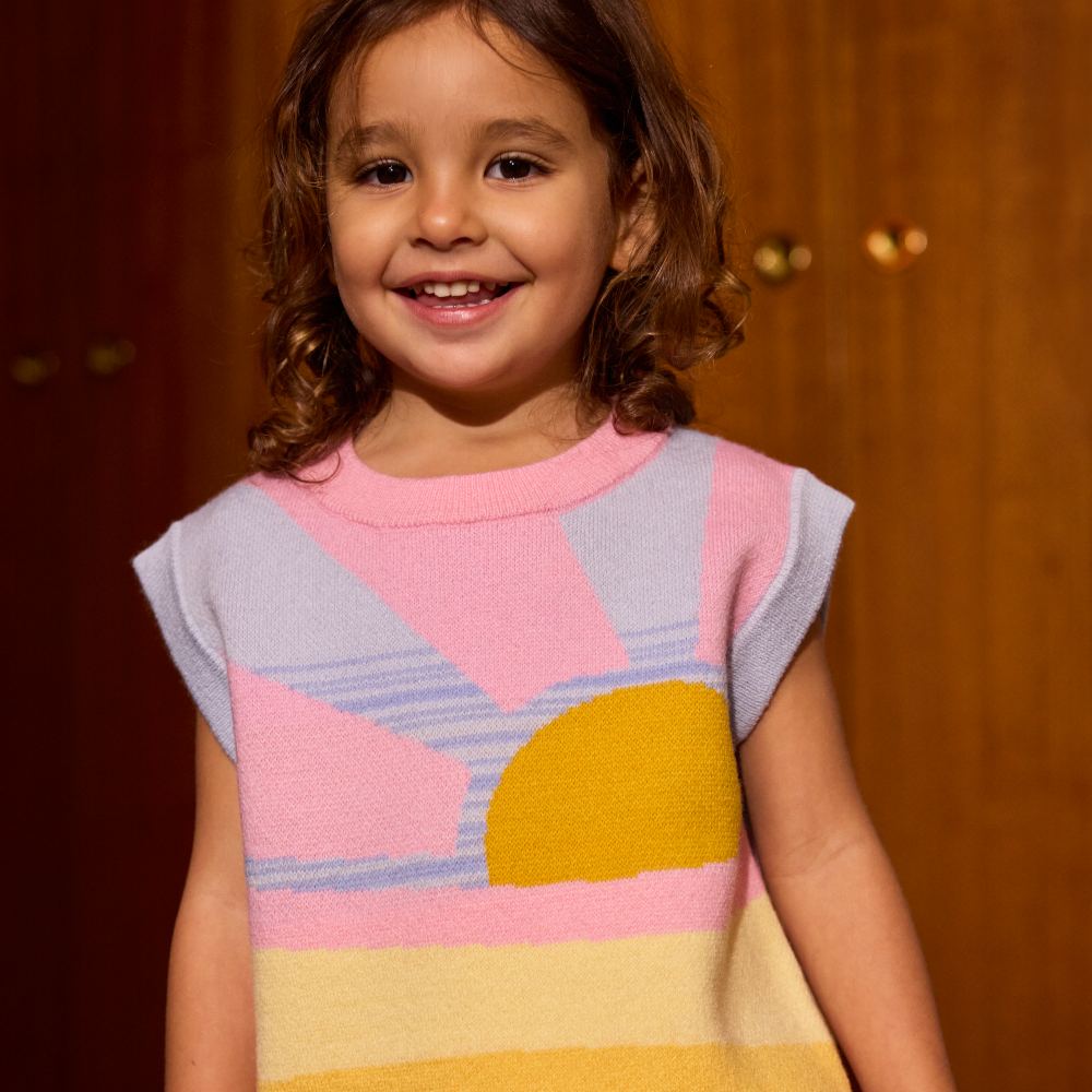 A young girl smiling at the camera wearing a summer top with a sun motif 