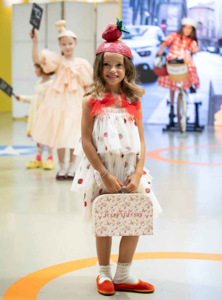A girl on stage in a white and red dress holding a small case 