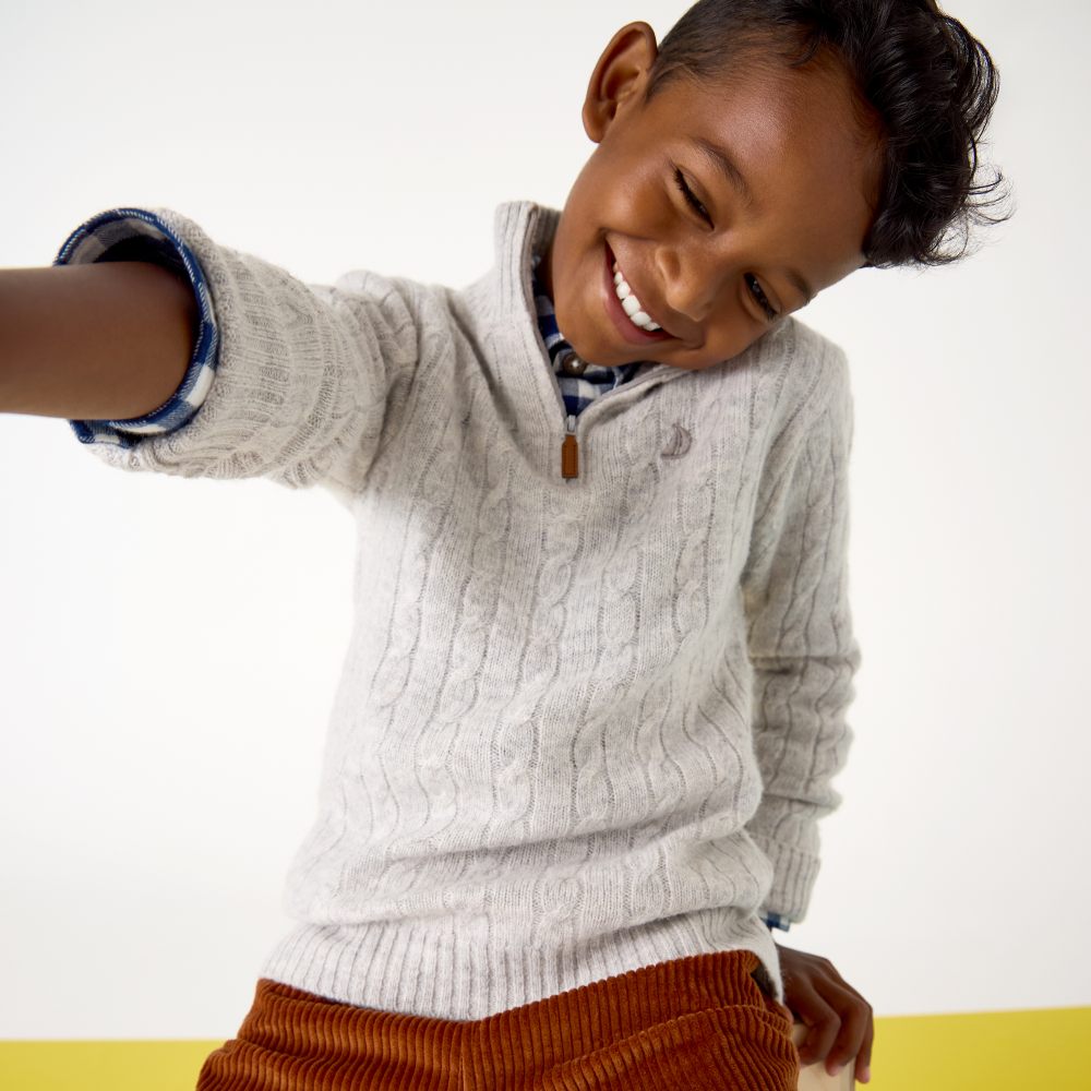 A smiling boy reaching forwards wearing a knitted jumper and cord trousers from the JoJo Junior collection 