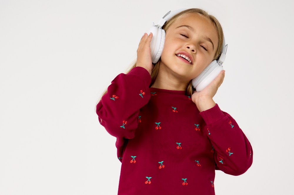 A girl wearing white headphones and a red cherry motif jumper from the JoJo Junior range
