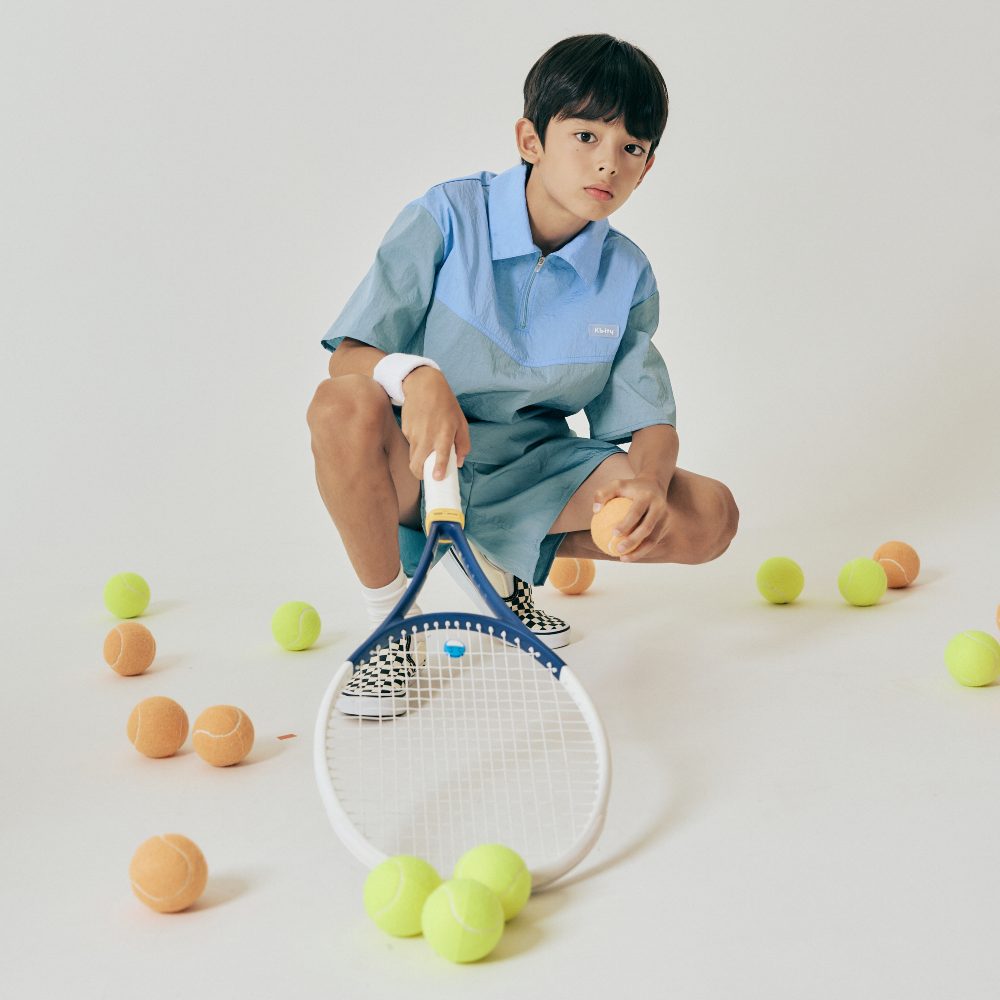 A boy holding a tennis racket knelt down on the floor around tennis balls 