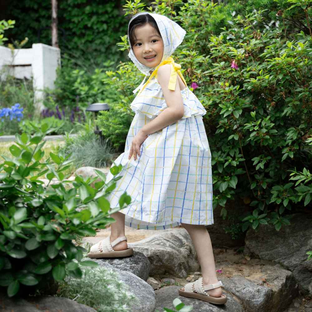 A young girl walking up some steps outside wearing a headscarf, summer dress and sandals 