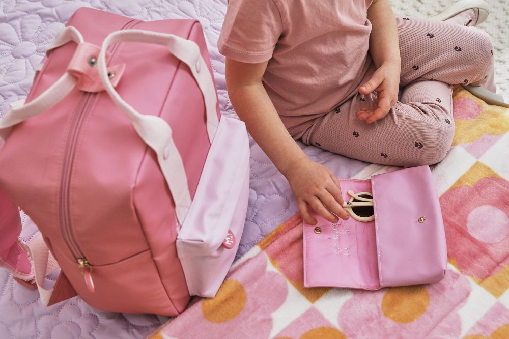 A child sat on a bed with a schoolbag by My 1st Years