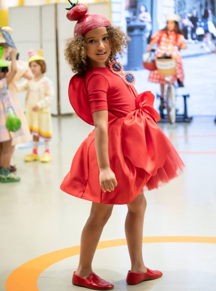 A girl in a red dress, shoes and hat in a fashion parade at Pitti Bimbo 101 