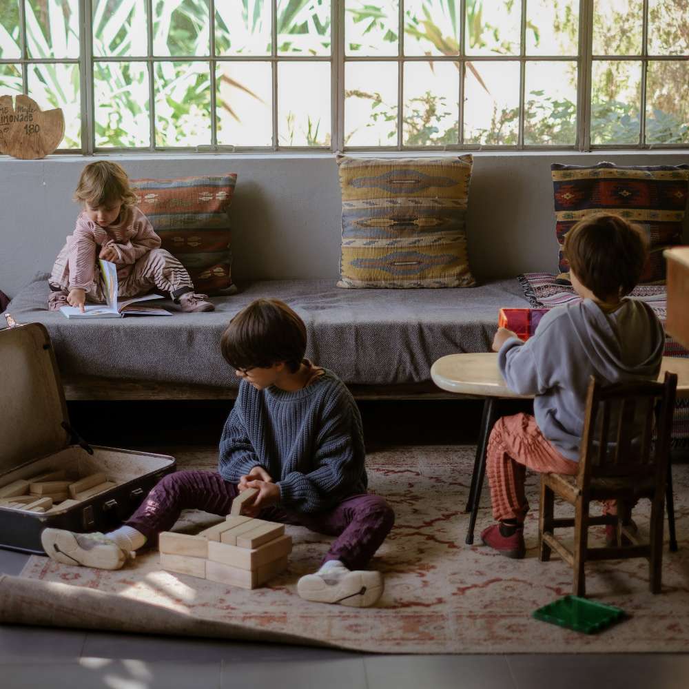 Children playing on the floor in a room wearing outfits by Petit Pli 