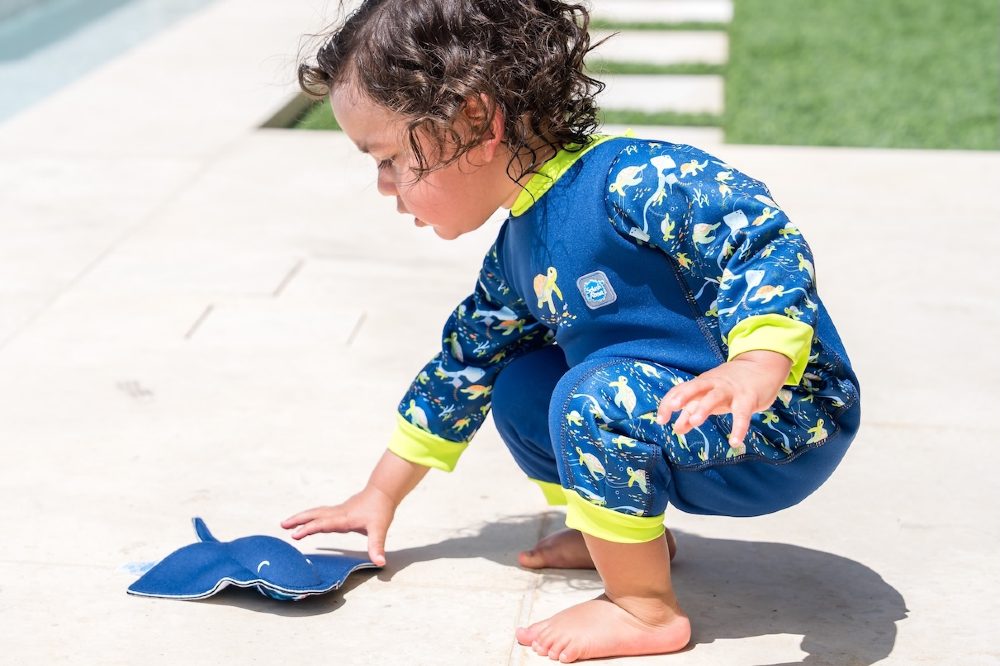 A young child crouched on the floor outside wearing a swimsuit by Splash About