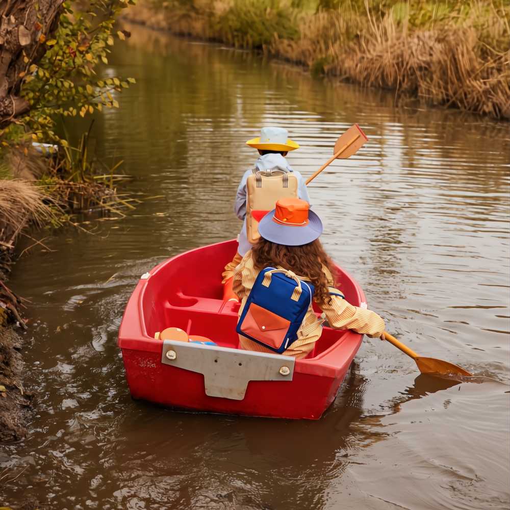 Two children in a red boat wearing hats and colourful backpacks 