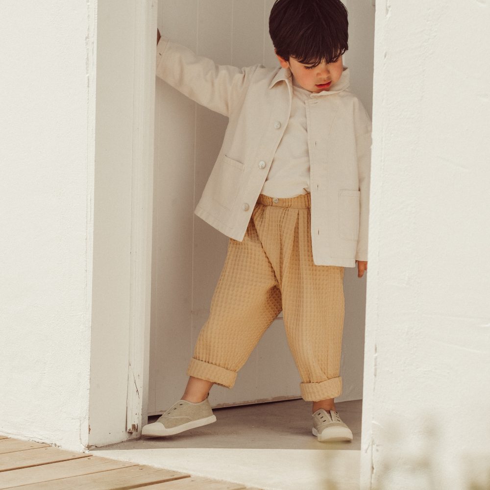 A young boy stood in a doorway wearing a summer jacket and trousers 