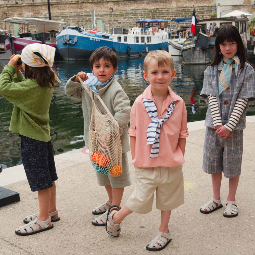 Four children in summer outfits stood in at the edge of a harbour 