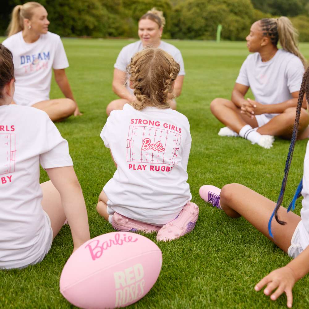 Three young girls sat together with three women on a ruby pitch