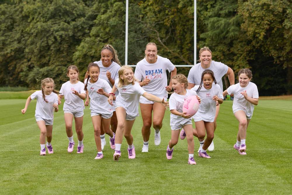 A group of women and girls running together on a rugby pitch