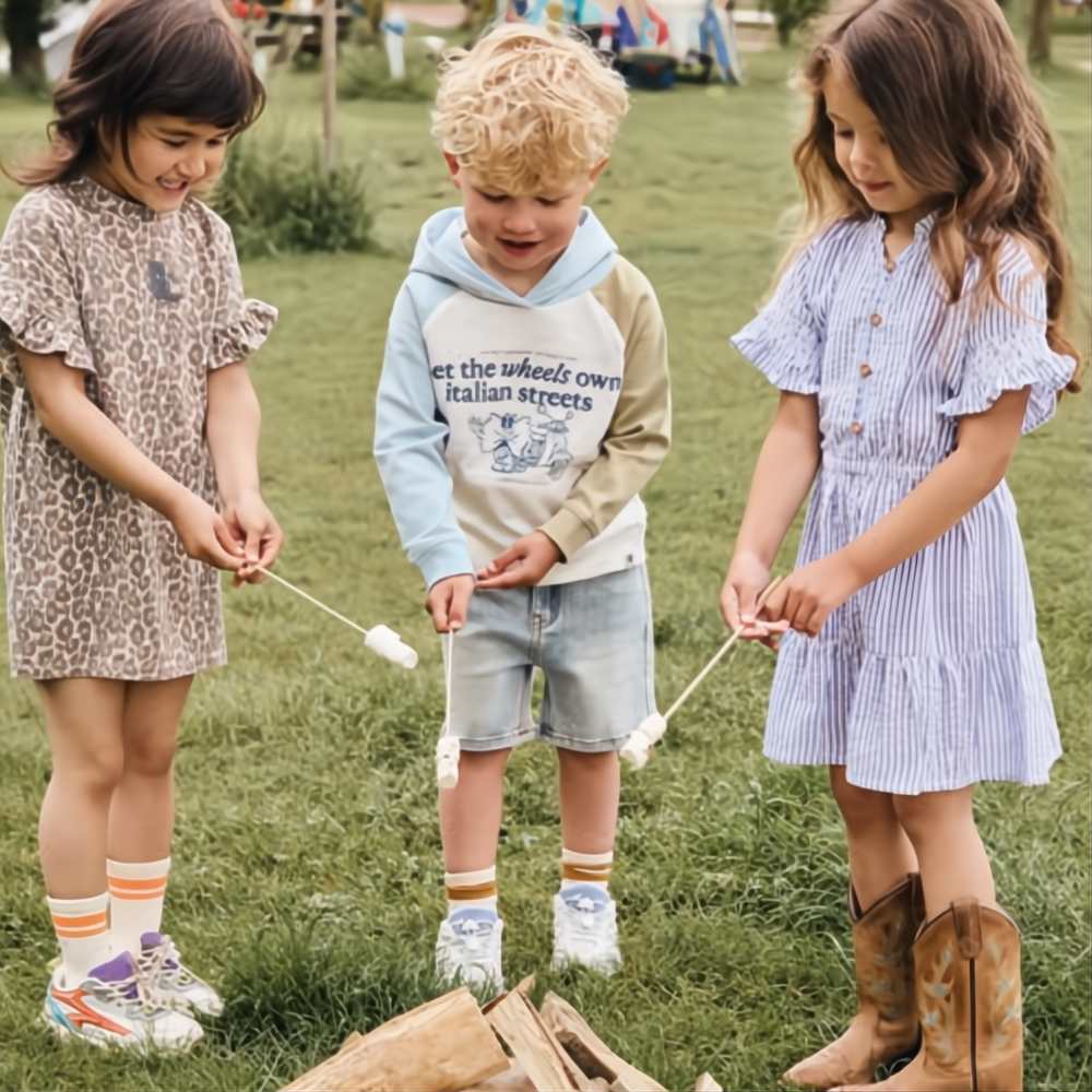 hree children in summer outfits stood outside toasting marshmallows