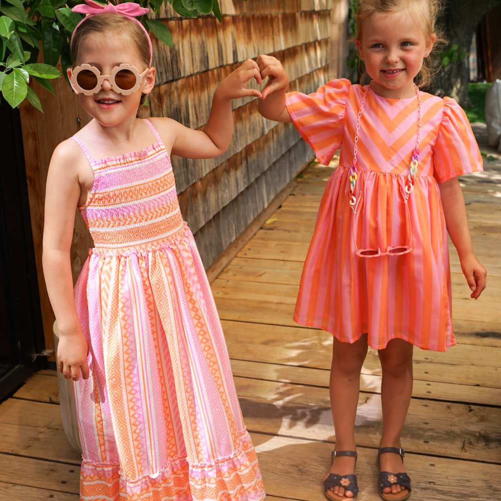 Two girls stood outside on wooden decking wearing bright sundresses
