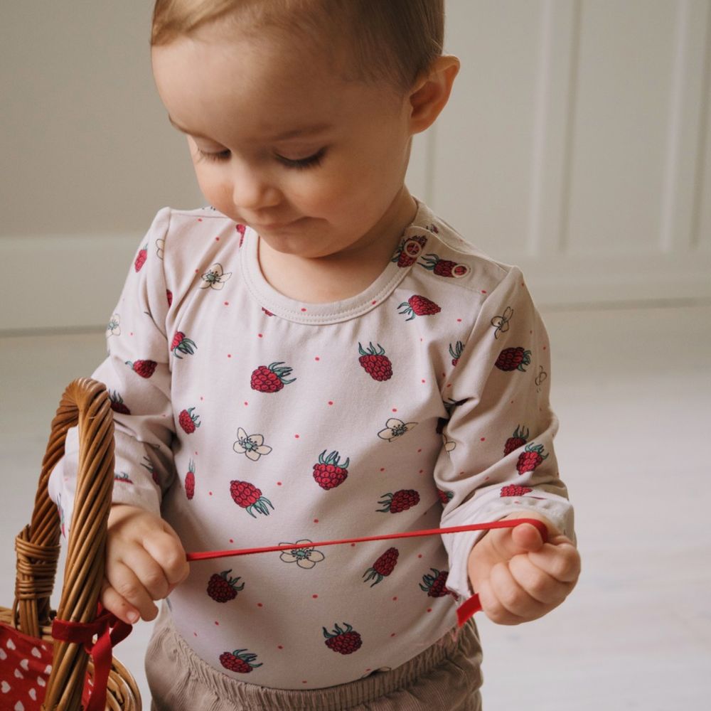 A young child beside a wicker basket wearing a raspberry and flower print top 