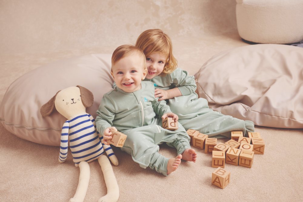 Two children sat on the floor amongst cushions and toys wearing sleepwear by Love to Dream