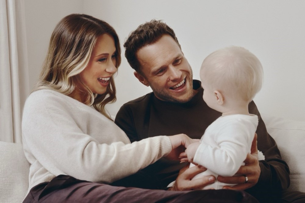 Olly Murs and Amelia Tank, the face of M&S's Parent Hood baby club, sat on a sofa smiling holding a baby