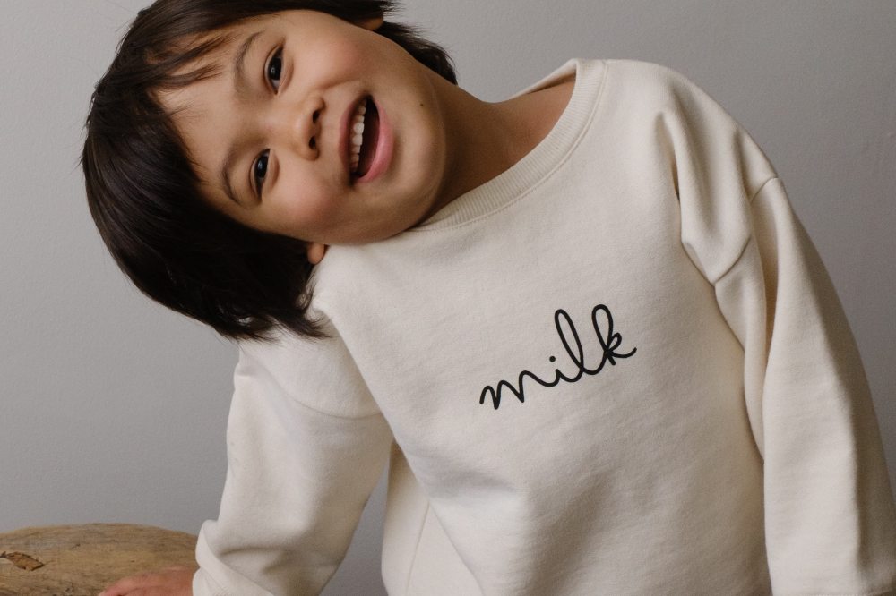A smiling child wearing a white top with Milk written on the front by Organic Zoo