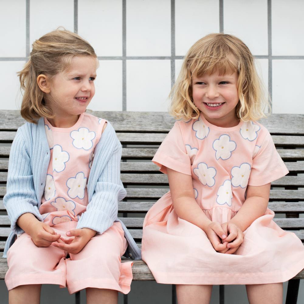 Two girls in floral motif summer outfits sat outside on a bench 