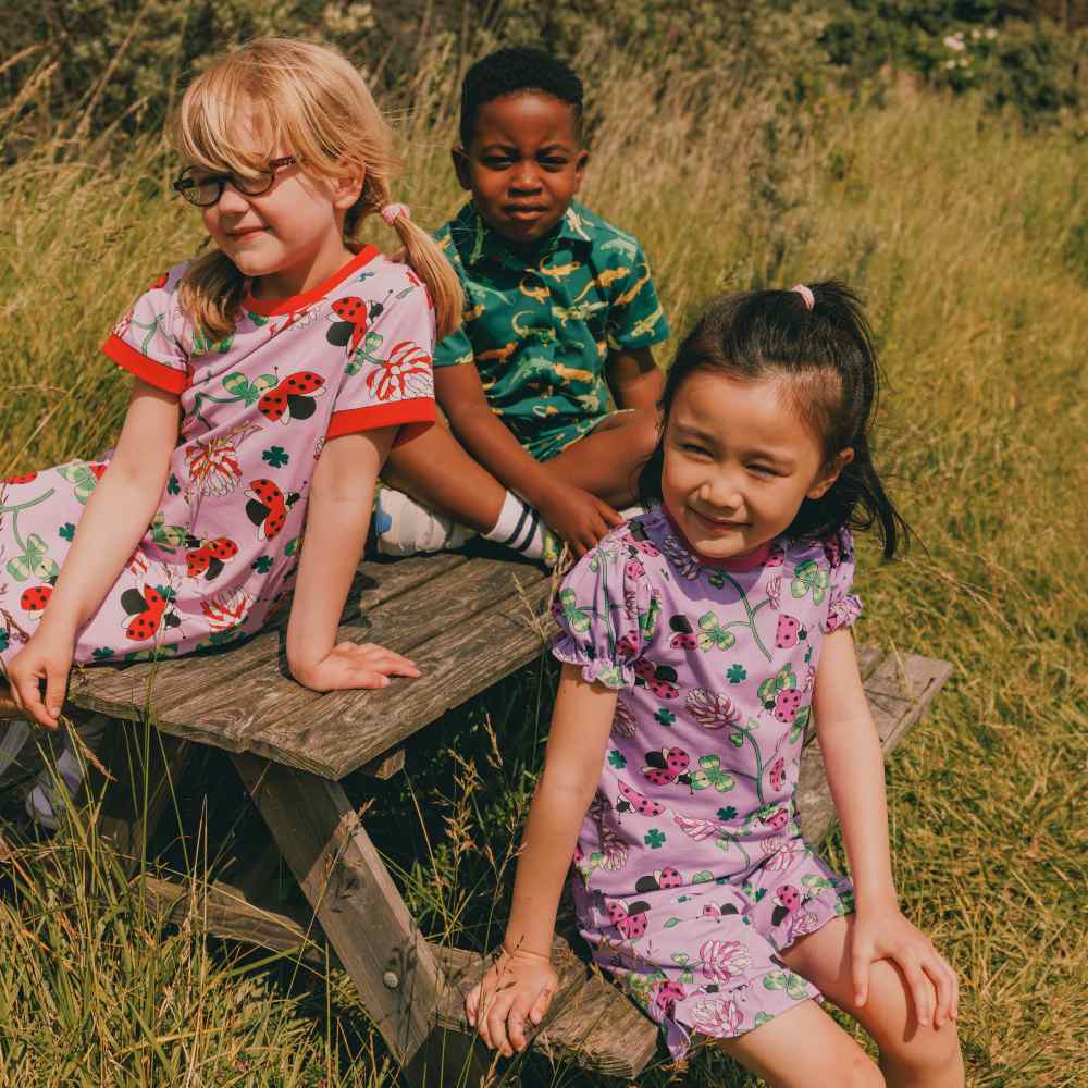 Three children in bright, printed summer outfits sat at a picnic table in a field 