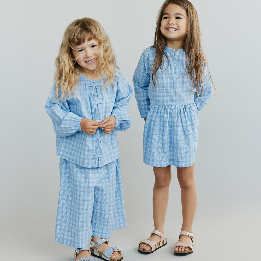 Two girls stood side by side wearing pale blue checked summer outfits 